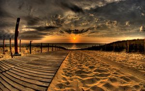 Preview wallpaper beach, sand, road, traces, fence, sun, evening, sky, decline, clouds