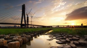 Preview wallpaper bridge, river, rocks, grass, city, building, sky, evening