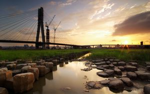 Preview wallpaper bridge, river, rocks, grass, city, building, sky, evening