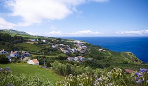 Preview wallpaper buildings, grass, hill, sea, sky, clouds