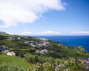 Preview wallpaper buildings, grass, hill, sea, sky, clouds