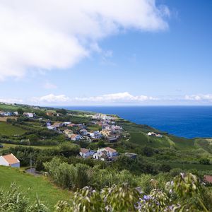 Preview wallpaper buildings, grass, hill, sea, sky, clouds