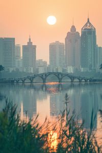 Preview wallpaper city, buildings, bridge, lake, sunset, sun