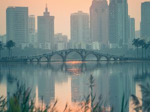 Preview wallpaper city, buildings, bridge, lake, sunset, sun