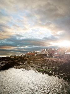 Preview wallpaper city, coast, stones, sun, light, sea, at home, clouds, cloudy