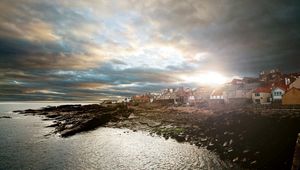 Preview wallpaper city, coast, stones, sun, light, sea, at home, clouds, cloudy