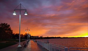 Preview wallpaper city, evening, sunset, sky, clouds, promenade, trees, benches, river, lights