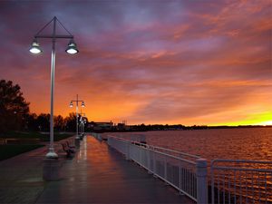 Preview wallpaper city, evening, sunset, sky, clouds, promenade, trees, benches, river, lights