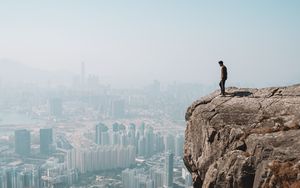 Preview wallpaper cliff, man, city, aerial view, height, loneliness