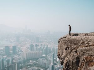 Preview wallpaper cliff, man, city, aerial view, height, loneliness