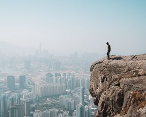 Preview wallpaper cliff, man, city, aerial view, height, loneliness