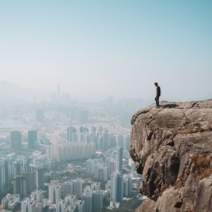 Preview wallpaper cliff, man, city, aerial view, height, loneliness