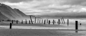 Preview wallpaper coast, pilings, sea, mountains, black and white