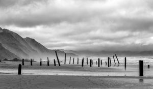 Preview wallpaper coast, pilings, sea, mountains, black and white