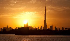 Preview wallpaper dubai, buildings, houses, silhouette, sunset, distance, sky, clouds, tower, water, stroking