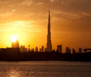 Preview wallpaper dubai, buildings, houses, silhouette, sunset, distance, sky, clouds, tower, water, stroking