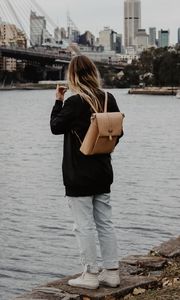 Preview wallpaper girl, backpack, loneliness, sad, shore, river, city