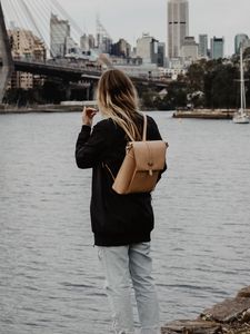 Preview wallpaper girl, backpack, loneliness, sad, shore, river, city