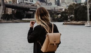 Preview wallpaper girl, backpack, loneliness, sad, shore, river, city