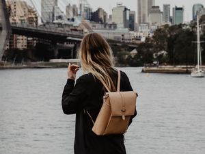 Preview wallpaper girl, backpack, loneliness, sad, shore, river, city