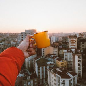 Preview wallpaper hand, mug, city, roofs, sundawn, rising sun