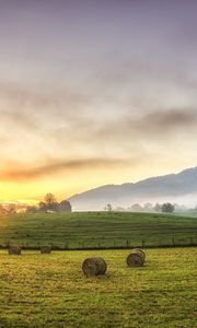 Preview wallpaper hay, bales, glade, sun, mountains, fog, trees, august, serenity
