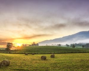 Preview wallpaper hay, bales, glade, sun, mountains, fog, trees, august, serenity
