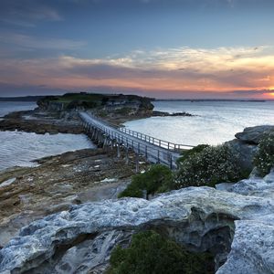 Preview wallpaper island, bridge, sea, stones, dusk