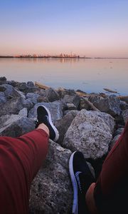 Preview wallpaper legs, sneakers, rocks, city, horizon, sea