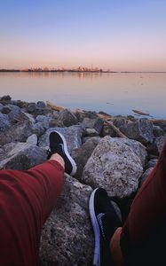 Preview wallpaper legs, sneakers, rocks, city, horizon, sea