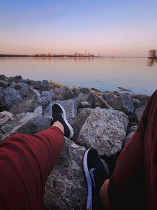 Preview wallpaper legs, sneakers, rocks, city, horizon, sea