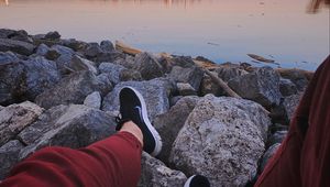 Preview wallpaper legs, sneakers, rocks, city, horizon, sea
