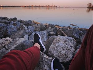 Preview wallpaper legs, sneakers, rocks, city, horizon, sea