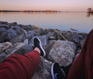 Preview wallpaper legs, sneakers, rocks, city, horizon, sea