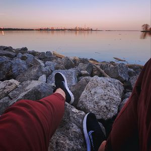 Preview wallpaper legs, sneakers, rocks, city, horizon, sea