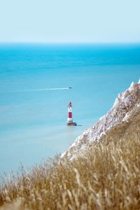 Preview wallpaper lighthouse, building, boat, sea, grass, horizon