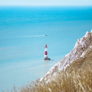 Preview wallpaper lighthouse, building, boat, sea, grass, horizon