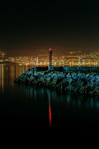 Preview wallpaper lighthouse, city, water, night, stones