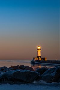 Preview wallpaper lighthouse, fire, stones, sea, twilight