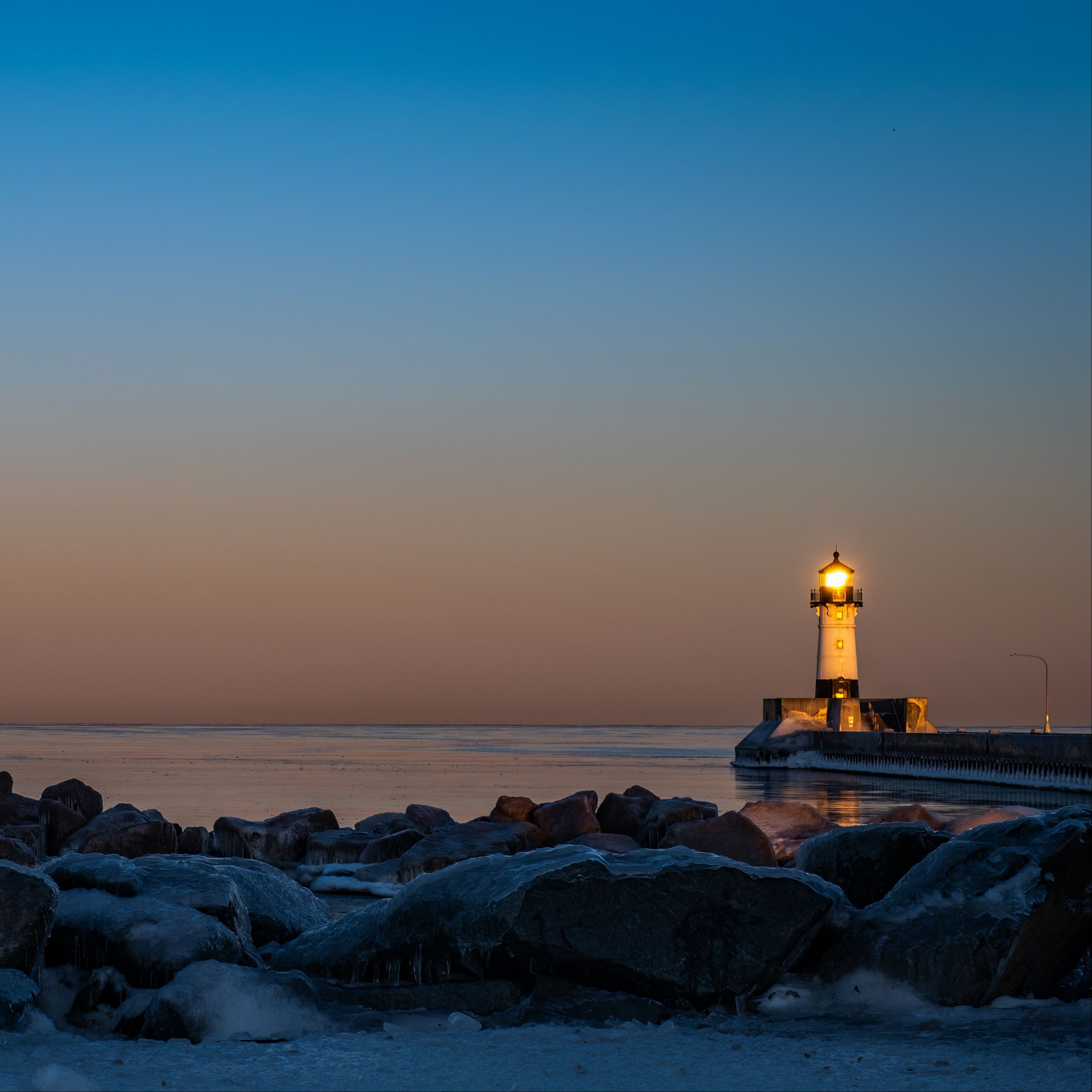 Download wallpaper 2780x2780 lighthouse, fire, stones, sea, twilight ...