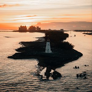 Preview wallpaper lighthouse, tower, island, sea, buildings, sunset