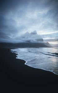 Preview wallpaper lonely, sea, beach, wave, sand, black, man, mountains, clouds