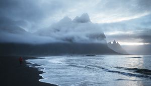 Preview wallpaper lonely, sea, beach, wave, sand, black, man, mountains, clouds