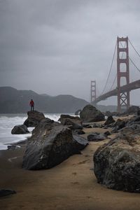 Preview wallpaper man, alone, rocks, waves, shore, bridge