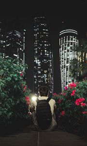 Preview wallpaper man, buildings, skyscrapers, bushes, flowers, night