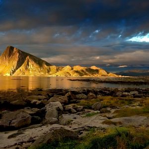 Preview wallpaper mountain, lighting, protected, stony, grass, sky, clouds, dense, gleam