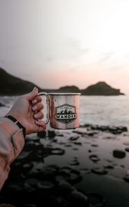 Preview wallpaper mug, hand, water, rocks, sunset