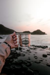 Preview wallpaper mug, hand, water, rocks, sunset