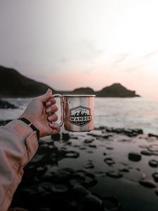 Preview wallpaper mug, hand, water, rocks, sunset