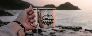 Preview wallpaper mug, hand, water, rocks, sunset